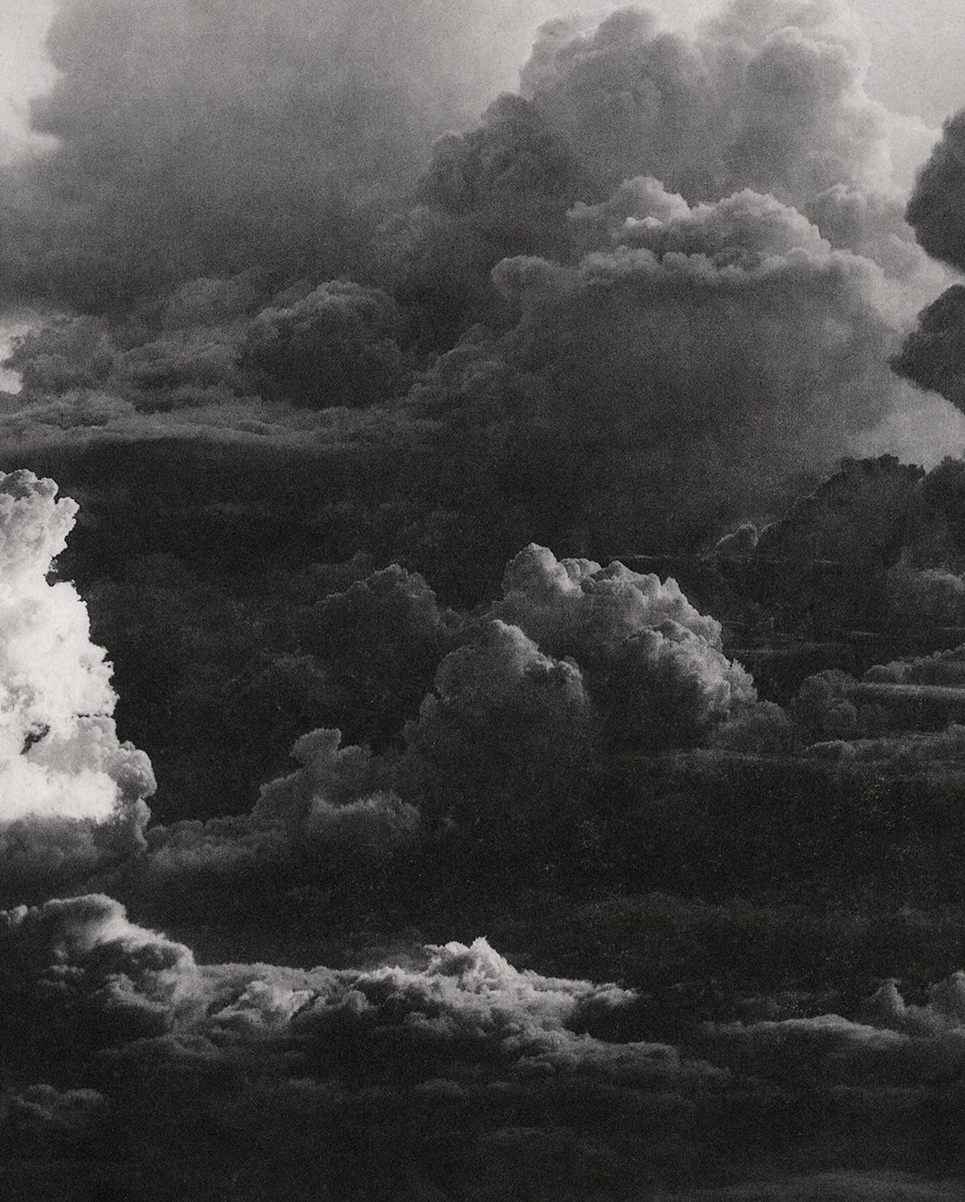 Dramatic black and white cloudscape with layered cloud formations filling the frame, creating a textured and atmospheric sky.