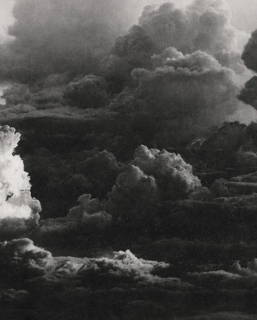 Dramatic black and white cloudscape with layered cloud formations filling the frame, creating a textured and atmospheric sky.