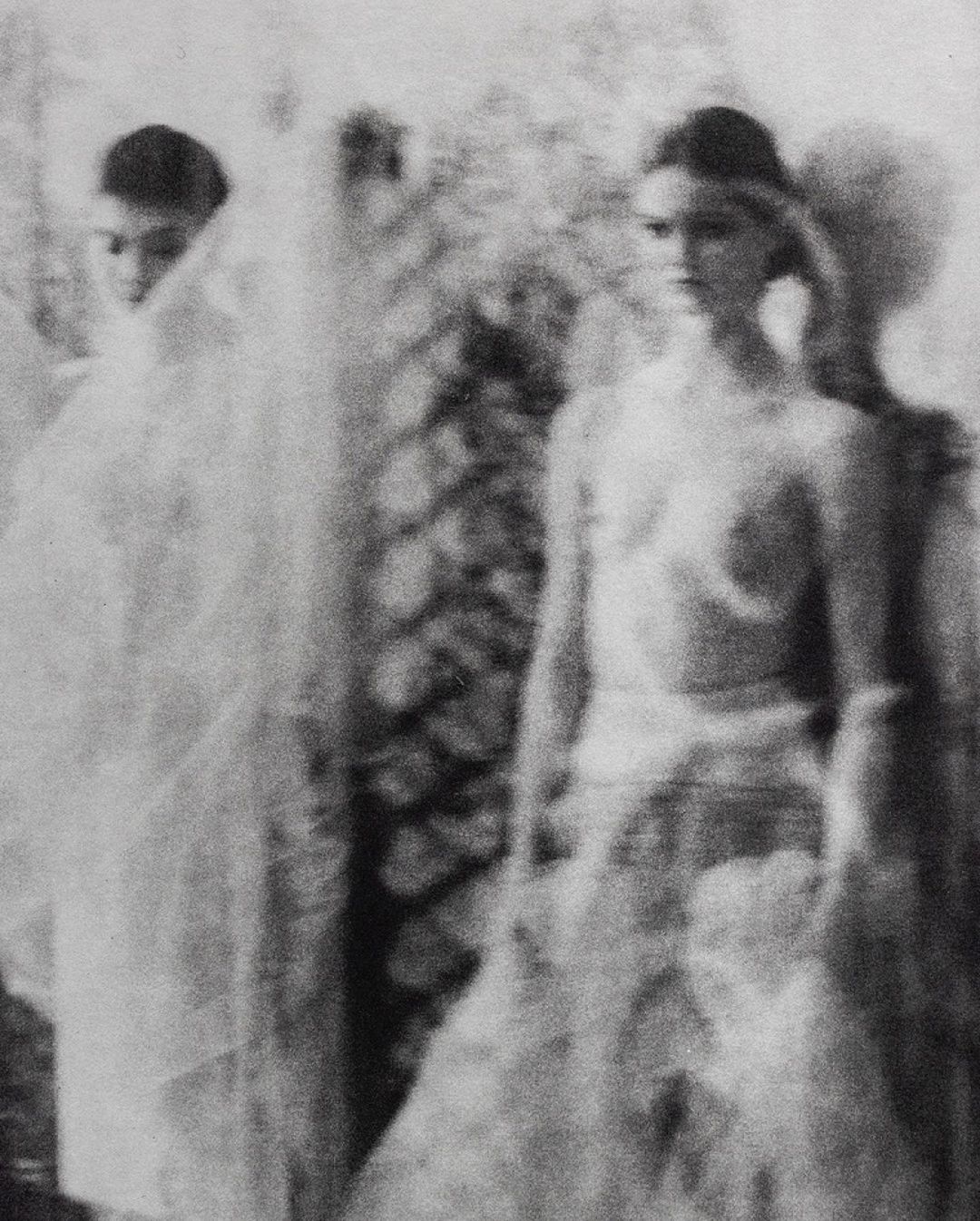 Two women in blurred black and white fashion portrait. One faces forward, the other is covered in white translucent material.
