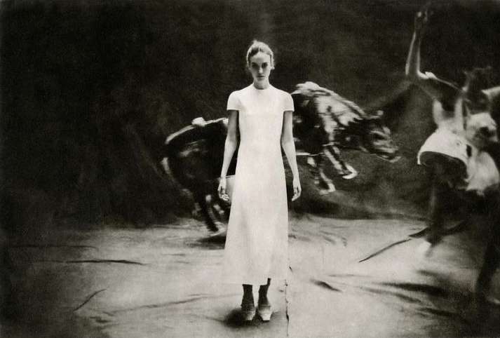 A surreal, slightly blurred fine art photography image of a standing female fashion model in front of dancers in motion and a wild boar.