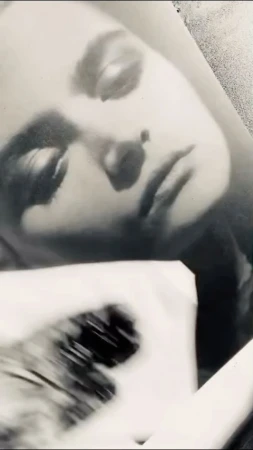 Monochrome portrait of a fair-skinned adult woman with closed eyes and dark eye makeup in a photograph-like image.