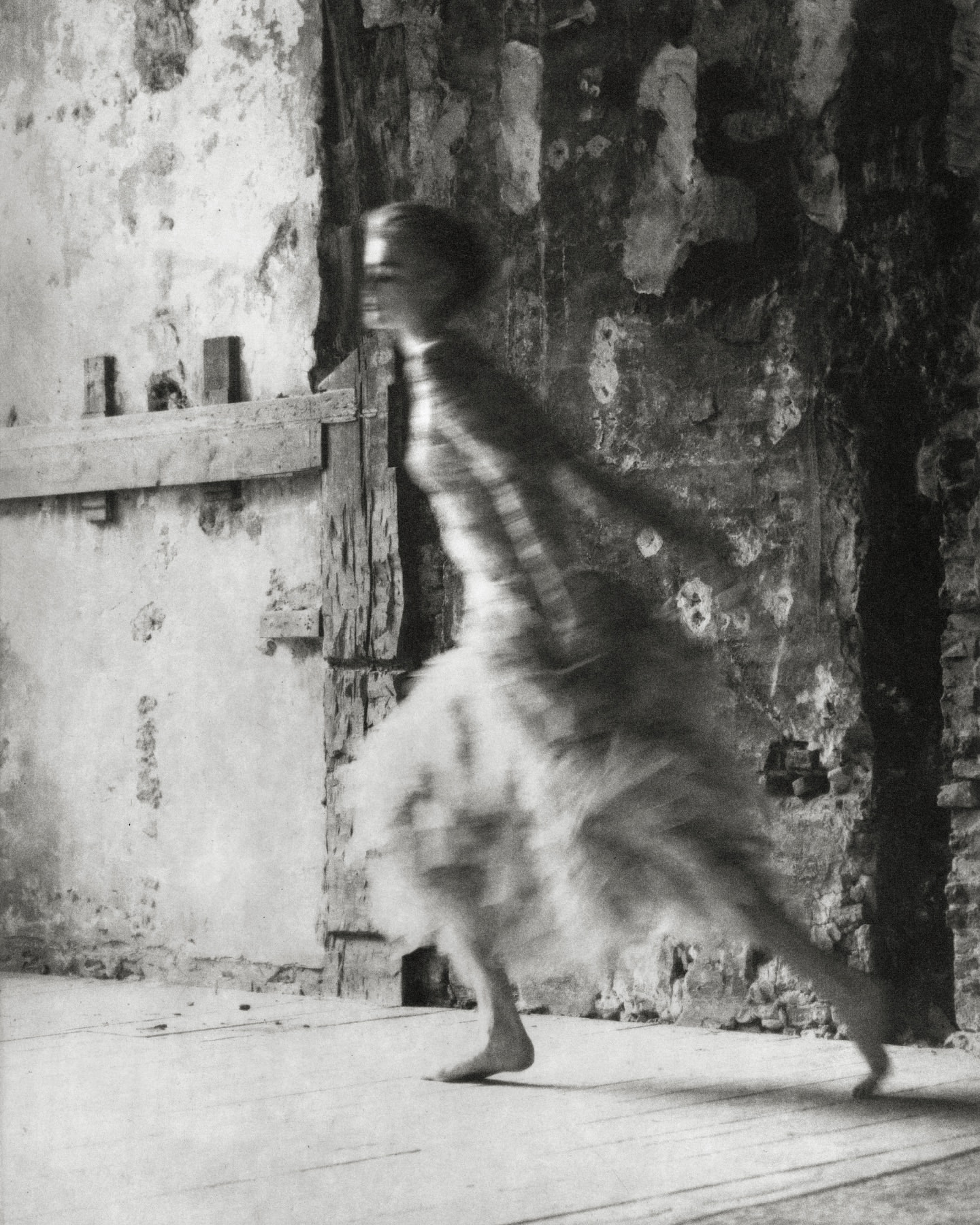 Blurred artistic photo of a woman in motion near a textured wall, showcasing motion blur, vintage style, and fine art photography.
