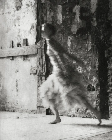 Blurred artistic photo of a woman in motion near a textured wall, showcasing motion blur, vintage style, and fine art photography.