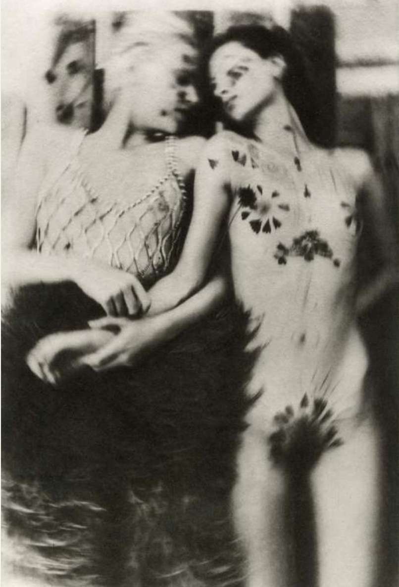 Monochrome photograph of two women in an indoor setting. One woman has dark body art. The photograph has soft focus and vintage effect.