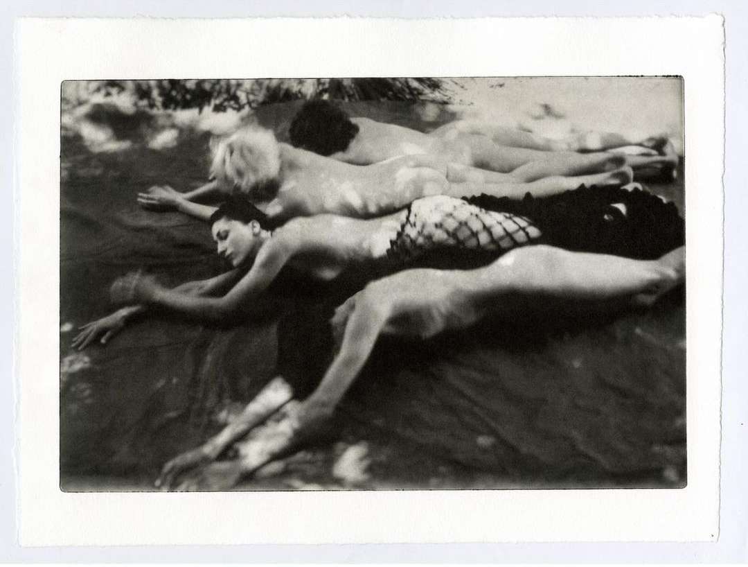 Black and white photograph of three women lying in a row with their arms stretched out, appearing relaxed and serene in soft lighting.