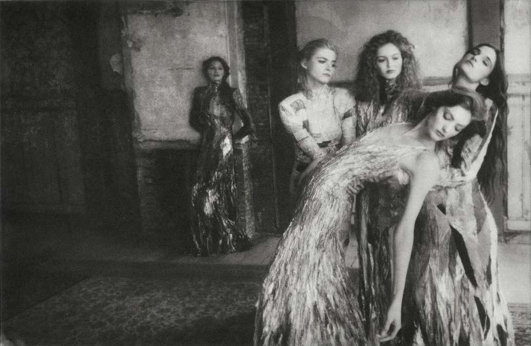 Monochrome art photography of a group of five women in elaborate gowns posing indoors with a dark and atmospheric environment. 