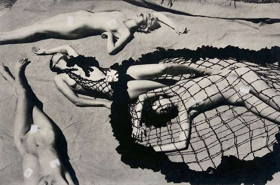 Monochrome image featuring four women lying on a neutral surface, posed artistically in a high-angle shot, with shadows and varying degrees of attire.