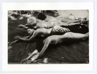 Four figures lying prone in a horizontal row on a dark surface, captured in a monochromatic photographic style.