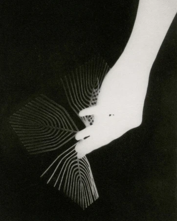 Monochrome rayogram featuring a hand holding patterned geometric paper against a black background by Chantal Elisabeth Ariens