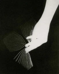 Monochrome rayogram featuring a hand holding patterned geometric paper against a black background by Chantal Elisabeth Ariens