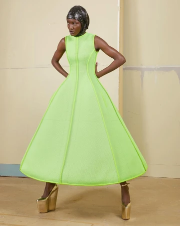 Fashion shot of a Black woman wearing a neon green dress with a matching head wrap and gold platform heels posing in a studio.