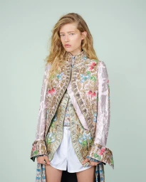 Portrait of a female model wearing an ornate embroidered floral coat against a pale green background