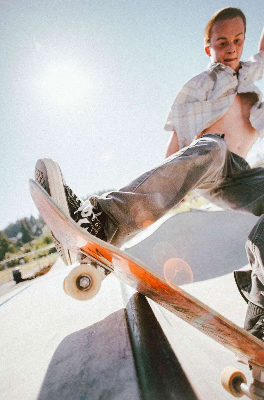 Young man skateboarding and performing a trick in an outdoor skatepark with a bright sunny day and blue sky in the background.