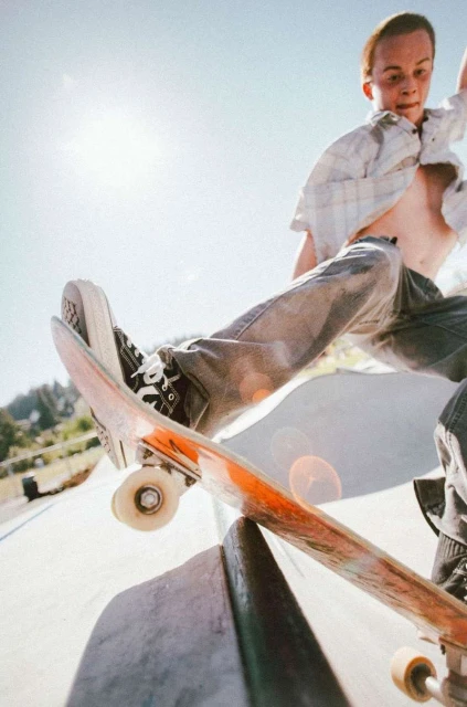 Young man skateboarding and performing a trick in an outdoor skatepark with a bright sunny day and blue sky in the background.