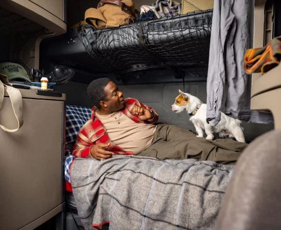 Man and Jack Russell Terrier resting in a truck cabin bed. Trucker relaxes with his dog in the sleeper berth of a semi-truck.