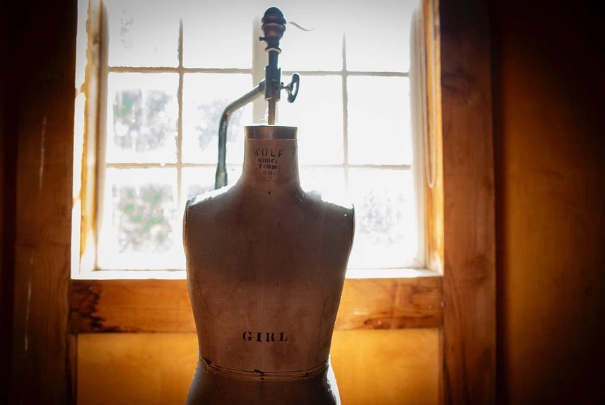 Vintage dress form in a room with window light. Rustic fashion industry, design, and tailoring concept. Antique mannequin display.