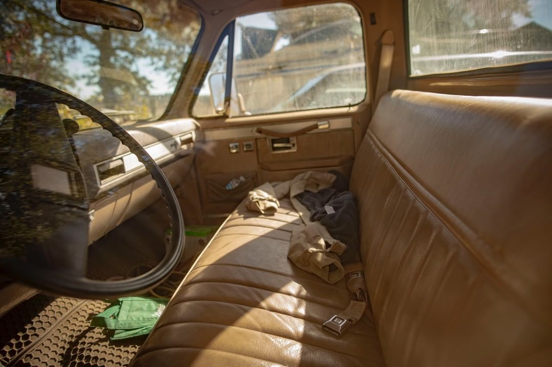 Pickup truck interior featuring tan vinyl upholstery, steering wheel view, and clothing items on the bench seat. The scene is naturally lit.