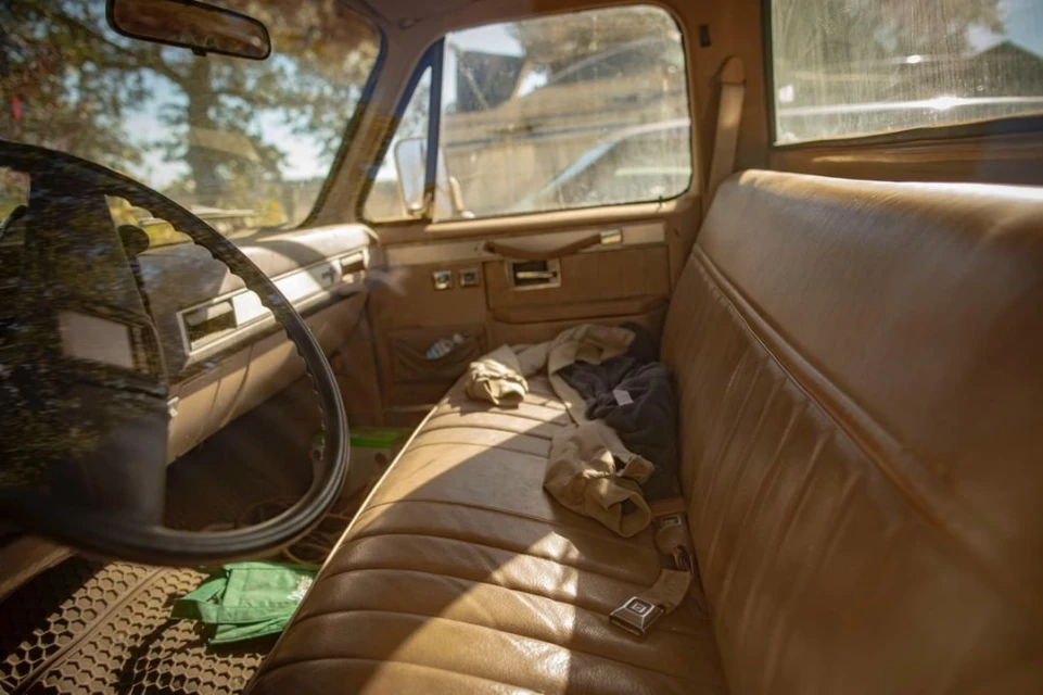 Pickup truck interior featuring tan vinyl upholstery, steering wheel view, and clothing items on the bench seat. The scene is naturally lit.