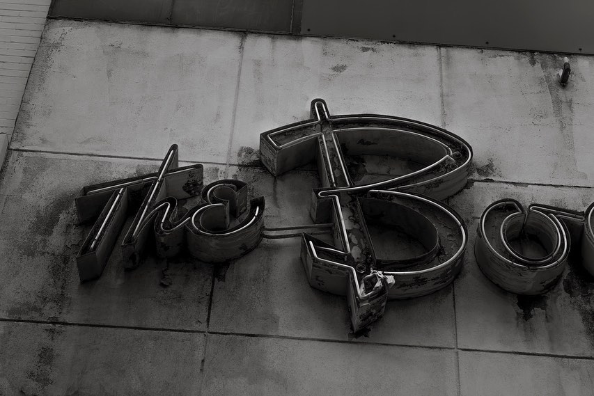 Monochrome image of weathered metal letters spelling out a word, mounted on a weathered wall, creating an industrial aesthetic.