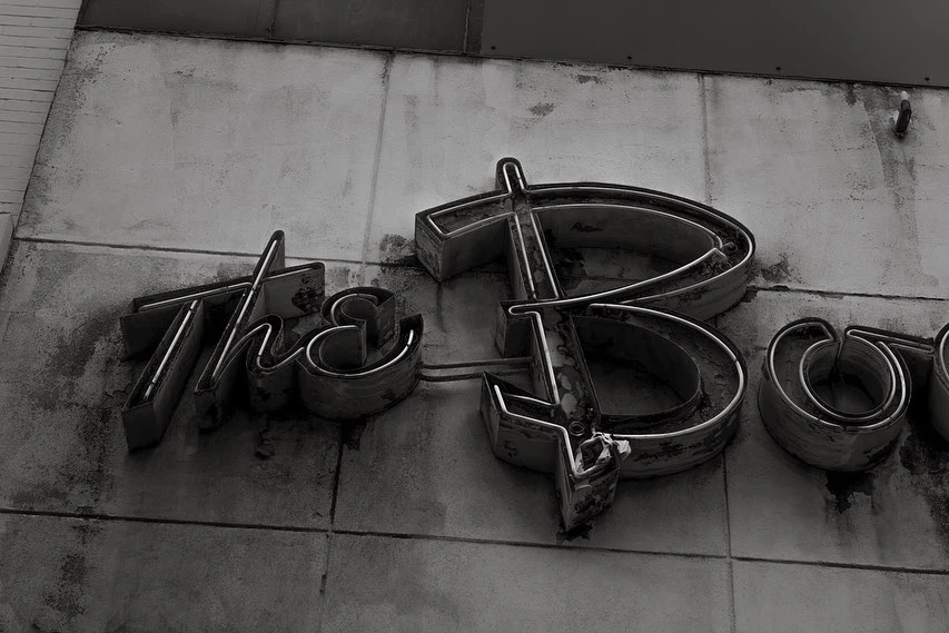 Monochrome image of weathered metal letters spelling out a word, mounted on a weathered wall, creating an industrial aesthetic.