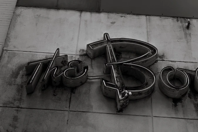 Monochrome image of weathered metal letters spelling out a word, mounted on a weathered wall, creating an industrial aesthetic.