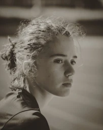 Portrait of a young woman with curly hair tied back looking off to the side in a monochrome shot by Charles Gullung