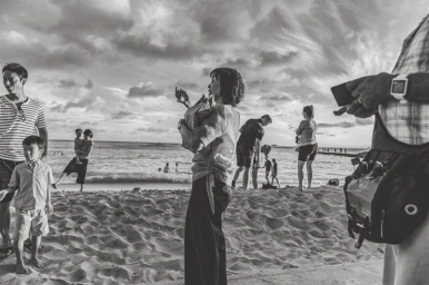 Black and white beach scene with a woman holding a bag in the center and people relaxing along the shore.