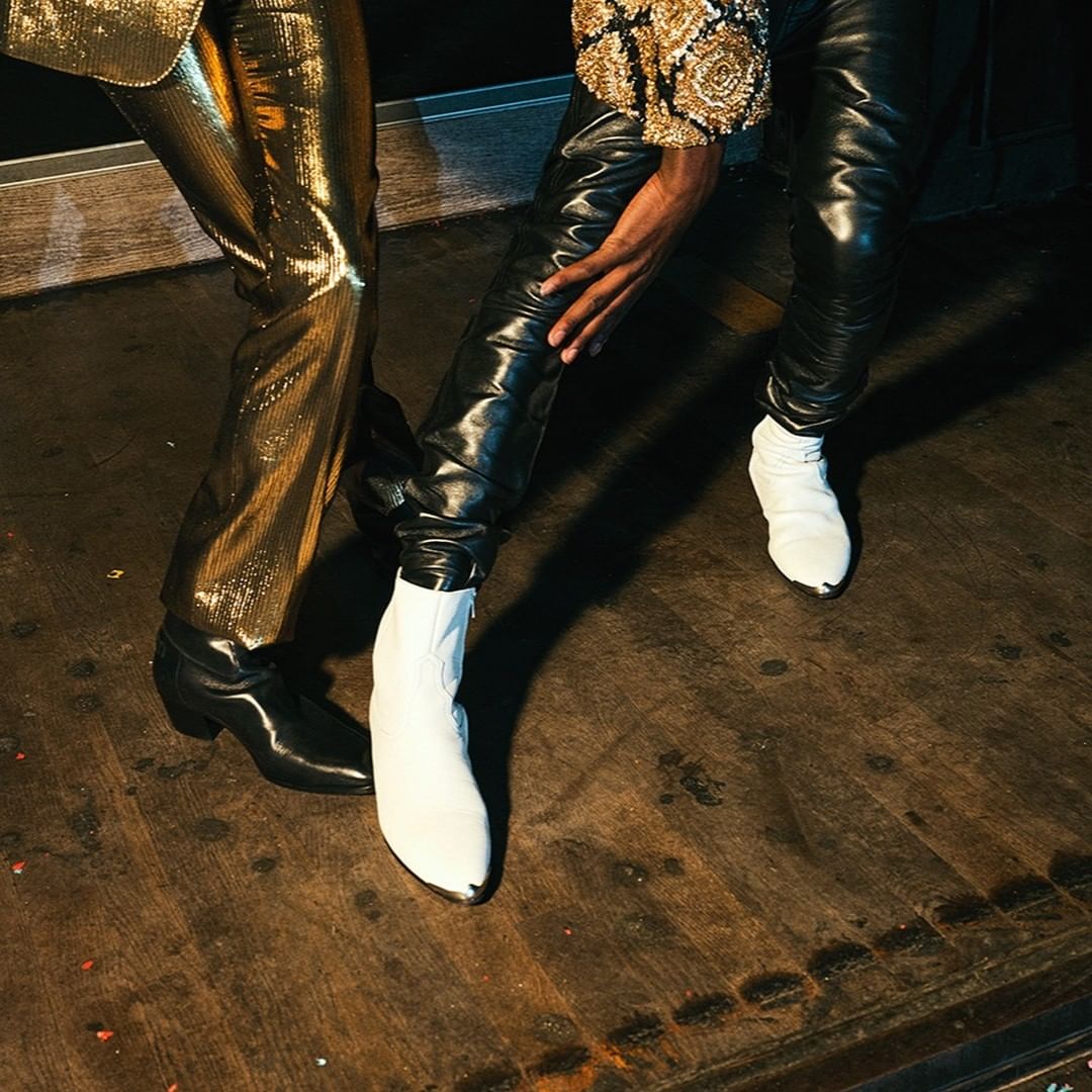 Close-up of two fashion models wearing shiny, textured pants and boots. One model wears gold pants and the other wears black leather pants.