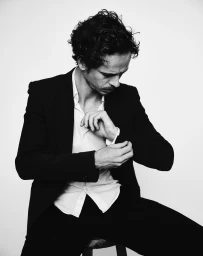 Man adjusting his cuff in a dark blazer and white shirt against a seamless white background