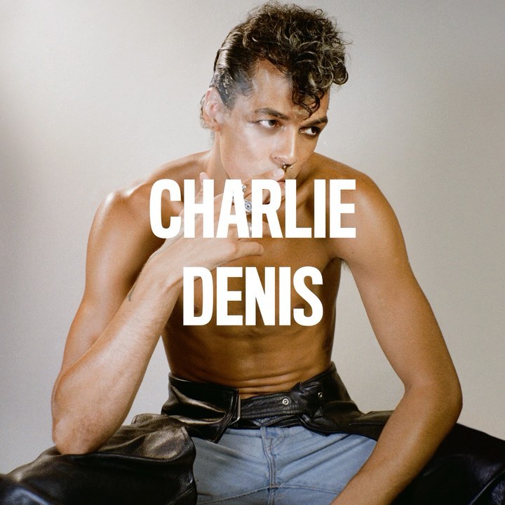 Close-up studio shot of a shirtless adult male model with styled hair, wearing jeans and black chaps. 