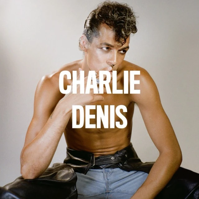 Close-up studio shot of a shirtless adult male model with styled hair, wearing jeans and black chaps. 