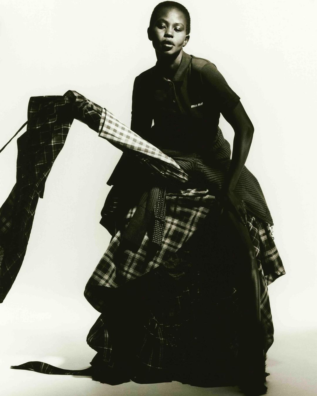 Elegant, dark-skinned woman posing in a dramatic layered plaid dress against a bright background, fashion-forward and artistic.