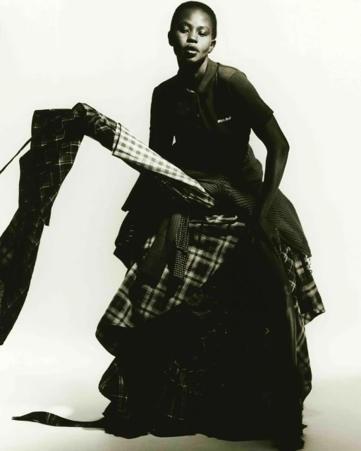 Elegant, dark-skinned woman posing in a dramatic layered plaid dress against a bright background, fashion-forward and artistic.