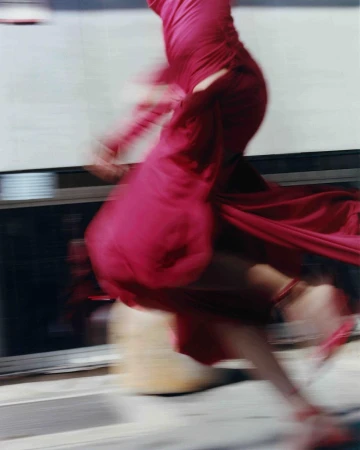 Fashion photography featuring a blurry, moving figure in a bright pink dress and matching high heels on a sidewalk, conveying motion and style.