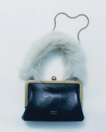 A black leather handbag with a plush white faux-fur handle and a thin golden metal chain strap against a plain white background.