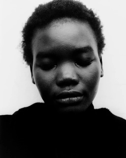 Close-up black and white portrait of an adult woman with short natural hair, looking down, against a plain white background in a minimalist style.