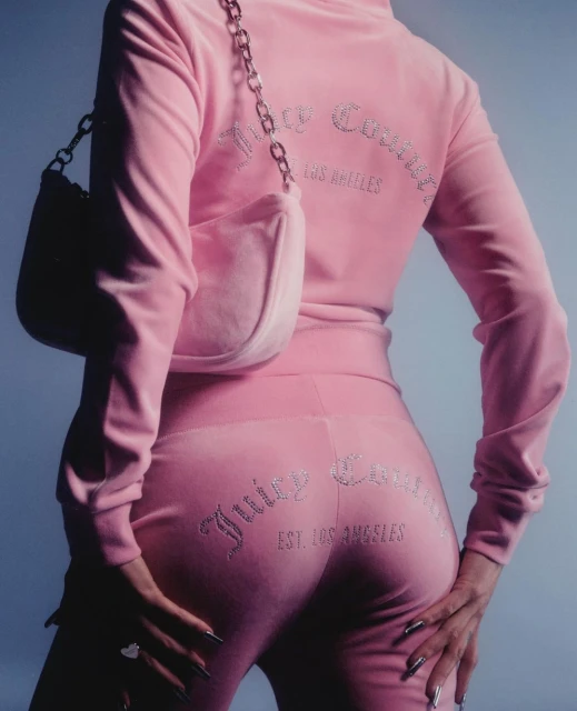 Back view of a woman wearing a pink Juicy Couture tracksuit with a matching pink shoulder bag, silver nails, and a ring.