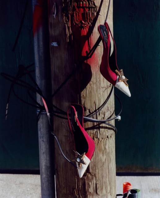 Stylish women's high heel shoes hanging from a weathered telephone pole with exposed wires in a unique outdoor fashion setting.