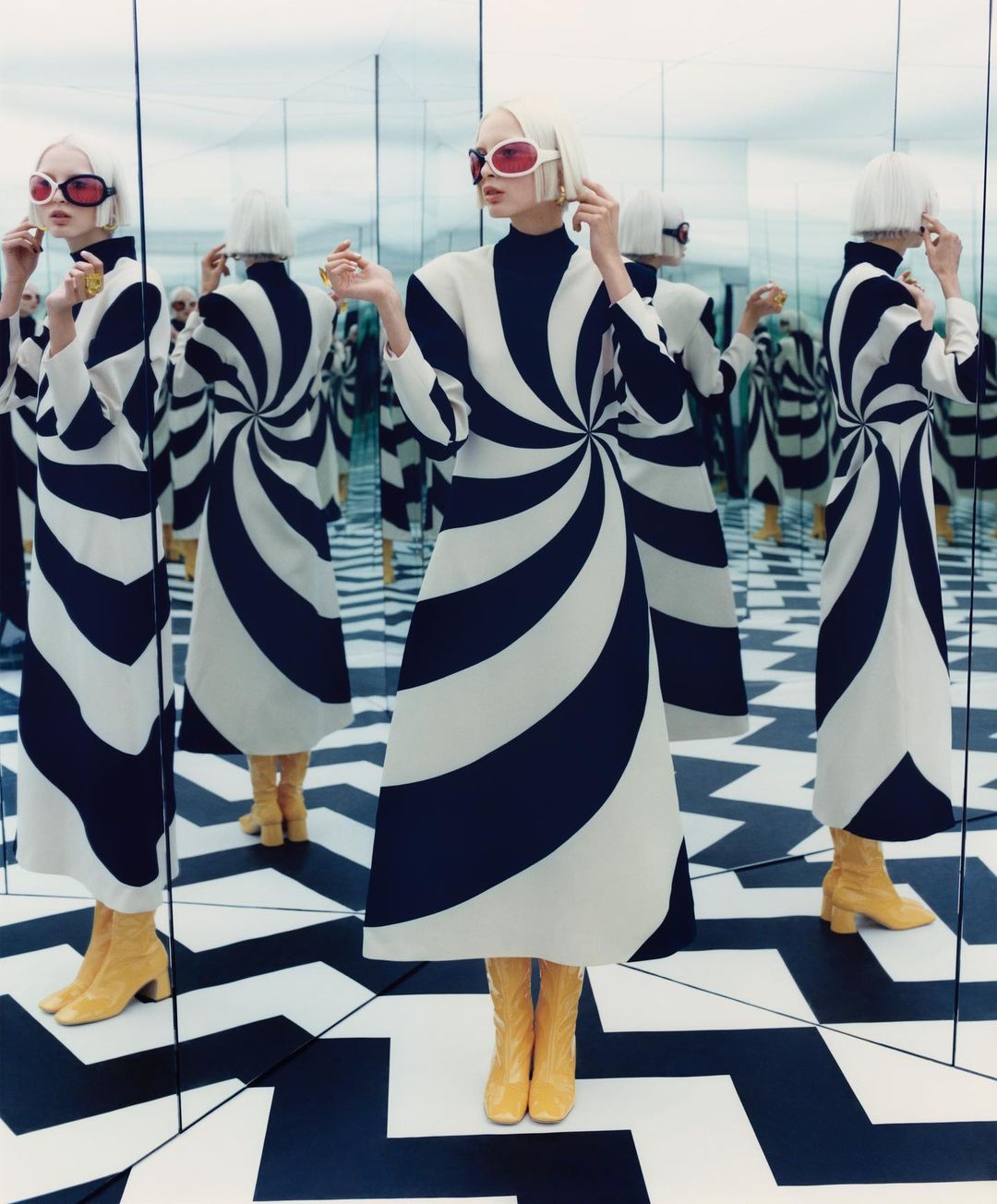 A fashion shot features a model in a black and white patterned dress, standing in a mirrored room, creating multiple reflections.