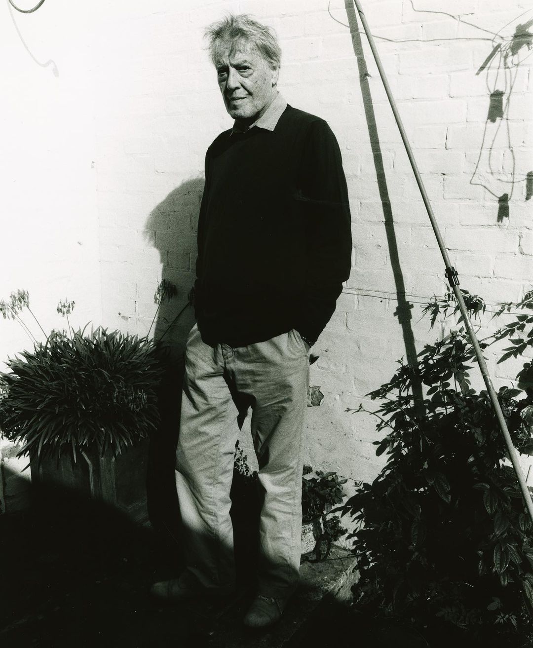 Portrait of an elderly man standing outdoors against a light brick wall by photographer Charlie Gates in London
