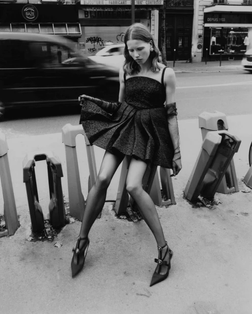 Monochrome fashion shot of a woman in a dress and heels posing on a city street, with blurred vehicles adding dynamic movement.