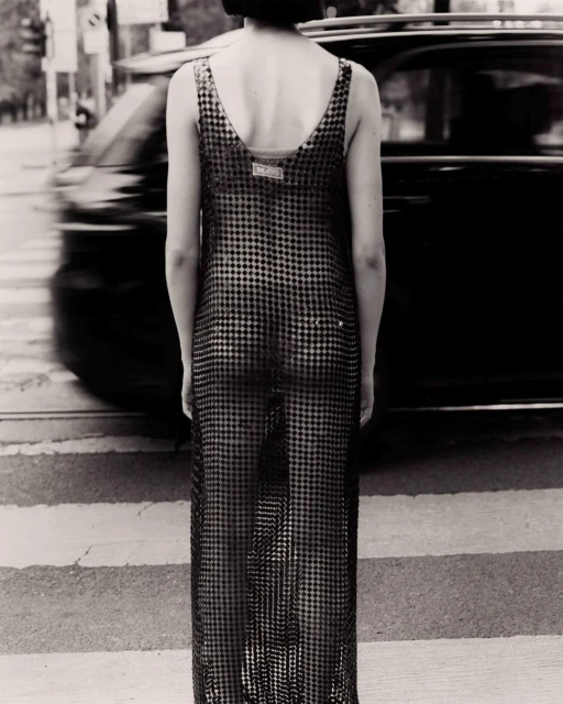 Adult female in maxi dress standing in a crosswalk in a monochrome fashion photograph with a vehicle passing by in the background.