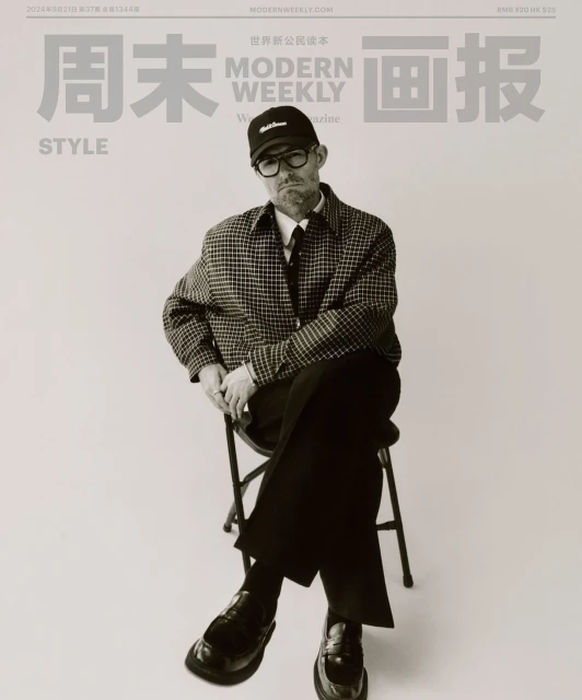 Modern Weekly magazine cover featuring an adult male wearing glasses, a cap, and a checkered jacket, seated on a metal stool.