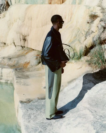 Man wearing a black leather jacket and green trousers standing by rocky mineral pools
