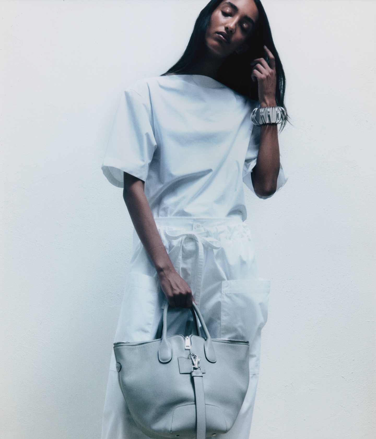 Woman in white outfit holding grey tote bag against a white background. Silver bracelet accentuates the minimalist fashion style.
