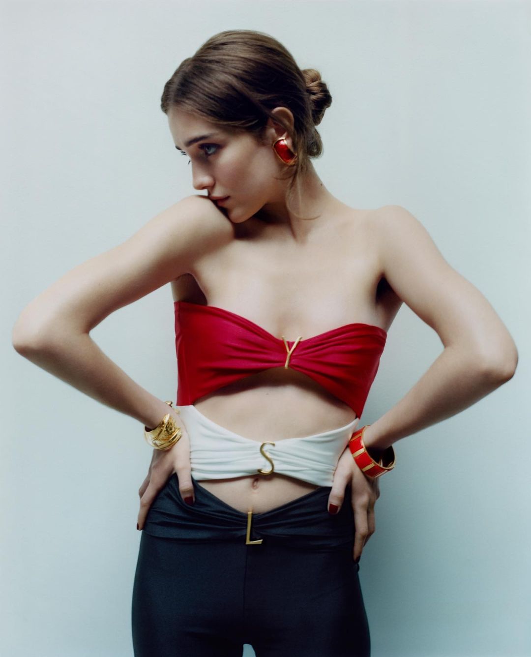Fashion shot of a woman in a red, white, and black outfit with jewelry, posing against a plain studio backdrop with soft lighting.