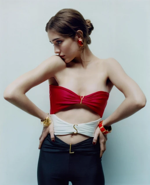 Fashion shot of a woman in a red, white, and black outfit with jewelry, posing against a plain studio backdrop with soft lighting.