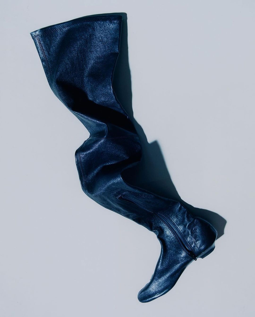 Over-the-knee high fashion boot in dark blue leather on light background in studio lighting for advertising and editorial use.