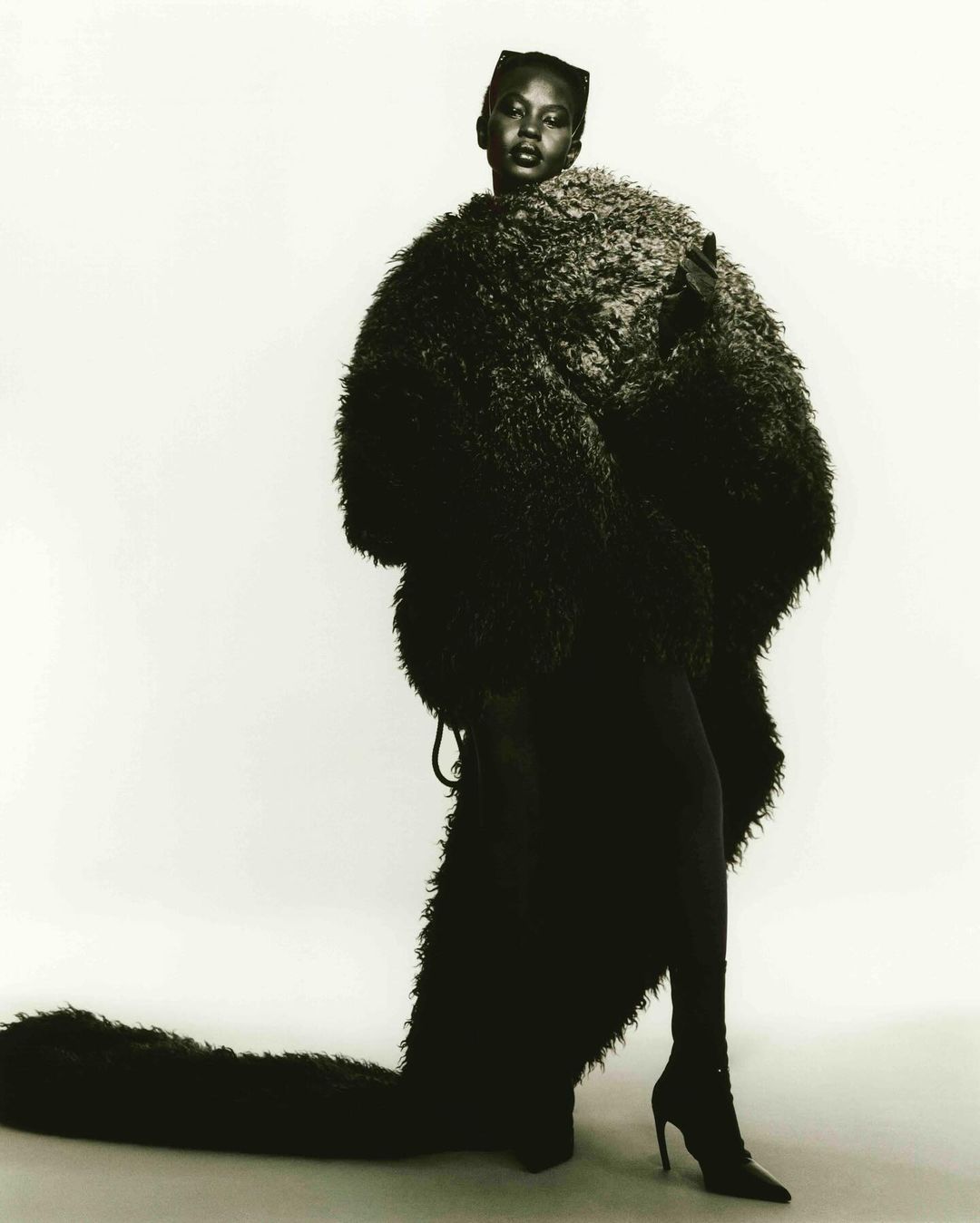 Fashion shot of a black female model posing in a fur coat and heels against a white background in a studio. Fashion photography.