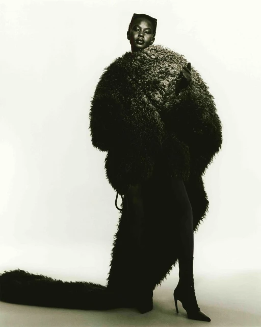 Fashion shot of a black female model posing in a fur coat and heels against a white background in a studio. Fashion photography.